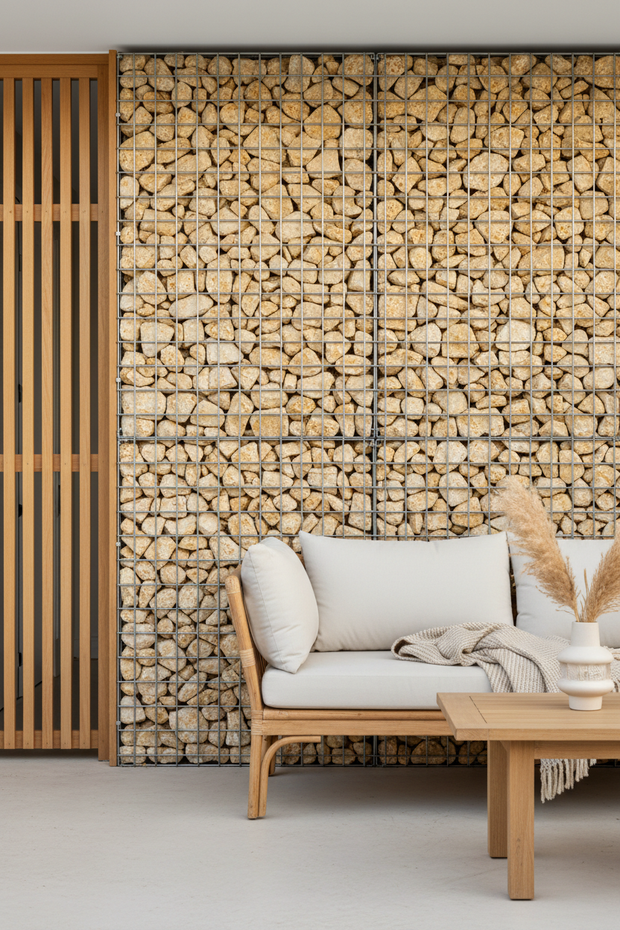 Portrait style architectural photograph of a high-end residential gabion feature wall, steel mesh filled with warm natural western australian limestone 100-150mm spalls, clean linear geometry, styled with cane lounge, light timber elements, minimalist coastal boho aesthetic, Perth home, calm and refined. DSLR, 35mm lens, f/4, ISO 100, 1/200s, natural light